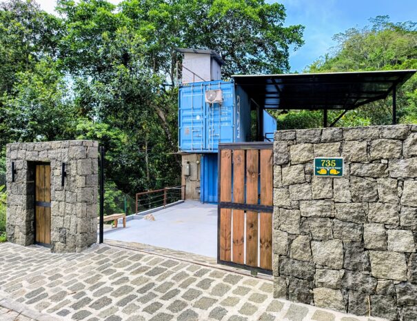 Entrada da propriedade: casa container em meio à mata, com portão e área de apoio — dentro de condomínio fechado com portaria 24h.